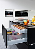 Mat black kitchen island and open drawers with dishes and utensils in kitchen
