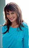 Portrait of pretty woman with brown hair and bangs wearing turquoise top, smiling