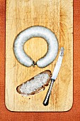 Palatinate liver sausage and a slice of bread spread with it on a wooden board with a knife (seen from above)