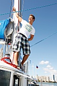 Man wearing plaid shorts, leaning and laughing on yacht