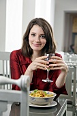 Pretty woman holding a glass of white wine with both hands in restaurant, smiling