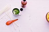 Raw noodle, spoon, lime slices in cup and sauce bottle on pink background 