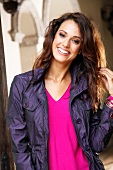 Portrait of happy woman with dark hair wearing purple jacket over pink v-neck top, smiling