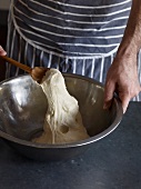 Close-up of hand mixing dough in bowl with wooden spoon