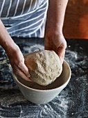 Close-up of hand putting dough in bowl for preparation of sourdough bread