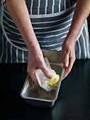 Close-up of hand greasing baking dish with butter