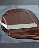 Melted chocolate being spread on baking paper using spatula, step 1