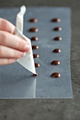 Dots of melted chocolate being made with piping bag, step 1