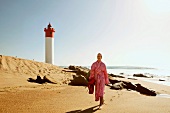 Woman in bathrobe walking on beach in front of lighthouse, Umhlanga, South Africa