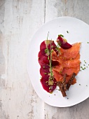 Marinated salmon trout with beetroot and spiced bread strips on plate, overhead view