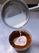 Adding heated milk to melted chocolate in bowl