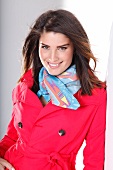 Portrait of attractive dark haired woman in red trench coat and colourful scarf, smiling