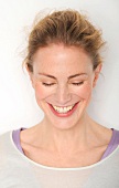 Close-up of happy woman wearing white top laughing with eyes closed