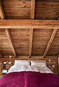 Bedroom with bed below sloping wooden ceiling