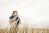 Woman wearing burberry coat standing relaxed between reeds on beach
