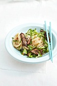 Noodle salad with sesame and beef on plate with chopsticks