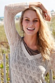 Portrait of pretty blonde woman wearing jumper with v neck standing on beach, smiling