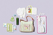 Diaper bag, changing mat and other baby care products on purple background