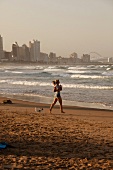 Woman jogging on beach with waves in sea at Durban, South Africa