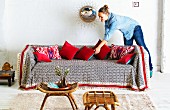 Woman arranging scatter cushions on sofa with colourful throw