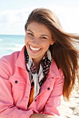 Dark-haired woman in a pink denim jacket, laughing by the sea