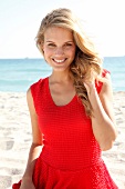 Portrait of attractive woman wearing red top standing on beach, smiling