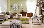 Pale chaise sofa, antique chest of drawers and bookcase with ladder in living room with pale green wall