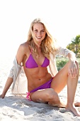 Portrait of blonde woman wearing pink bikini sitting on beach, smiling