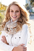 Pretty blonde woman in white jacket and scarf standing with arms crossed, smiling