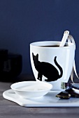 Close-up of coffee cup with cat motif and bowl of milk