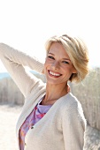 Portrait of pretty blonde woman with short hair wearing top and white cardigan, smiling
