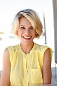 Portrait of happy blonde woman with short hair wearing yellow sleeveless top, smiling