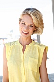 Portrait of happy blonde woman with short hair wearing yellow sleeveless top, smiling