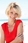 Portrait of pretty blonde woman with short hair wearing red top sitting on beach, smiling