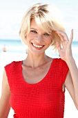 Portrait of pretty blonde woman with short hair wearing red top sitting on beach, smiling