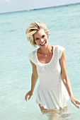 Portrait of happy blonde woman in white short dress enjoying in sea water, smiling