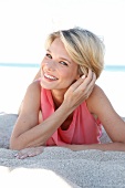 Portrait of beautiful blonde woman wearing pink top and shorts lying on sand, smiling