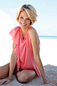 Portrait of happy woman wearing pink top sitting on sand, smiling