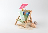 Rolled bill on deck chair with umbrella, shells and sand on white background
