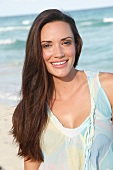 Portrait of beautiful woman with long dark hair wearing top and standing on beach, smiling