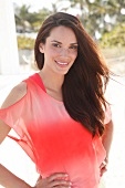 Portrait of beautiful woman with dark hair in red top standing with hands on hip, smiling