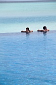 Man and woman relaxing in pool with sea in background in Dhigufinolhu Island, Maldives
