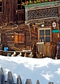 Chickens in snow in front of wooden hut