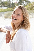 Portrait of beautiful blonde woman wearing white tunic blouse standing on beach, smiling