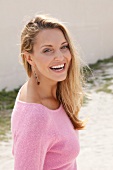 Portrait of beautiful blonde woman wearing pink sweater standing near wall, smiling