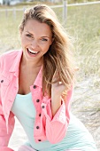Portrait of happy blonde woman with long hair wearing pink jacket, laughing