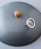 Wok lid with meat thermometer on gray background