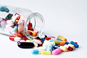 Close-up of colourful tablets and capsules spilled from jar on white background
