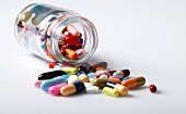 Close-up of glass jar with colourful tablets spilled on white background