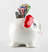 Close-up of white piggy bank with heart shaped ears and euro currencies